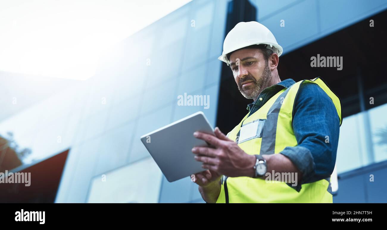 This software help me to keep track of everything. Shot of a engineer using a digital tablet on a construction site. Stock Photo