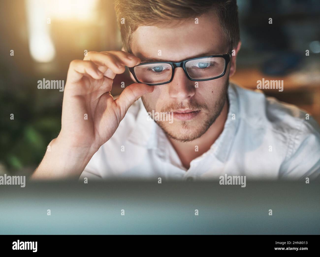 Am I seeing this right. Shot of a young designer adjusting his glasses as he looks at his computer screen. Stock Photo