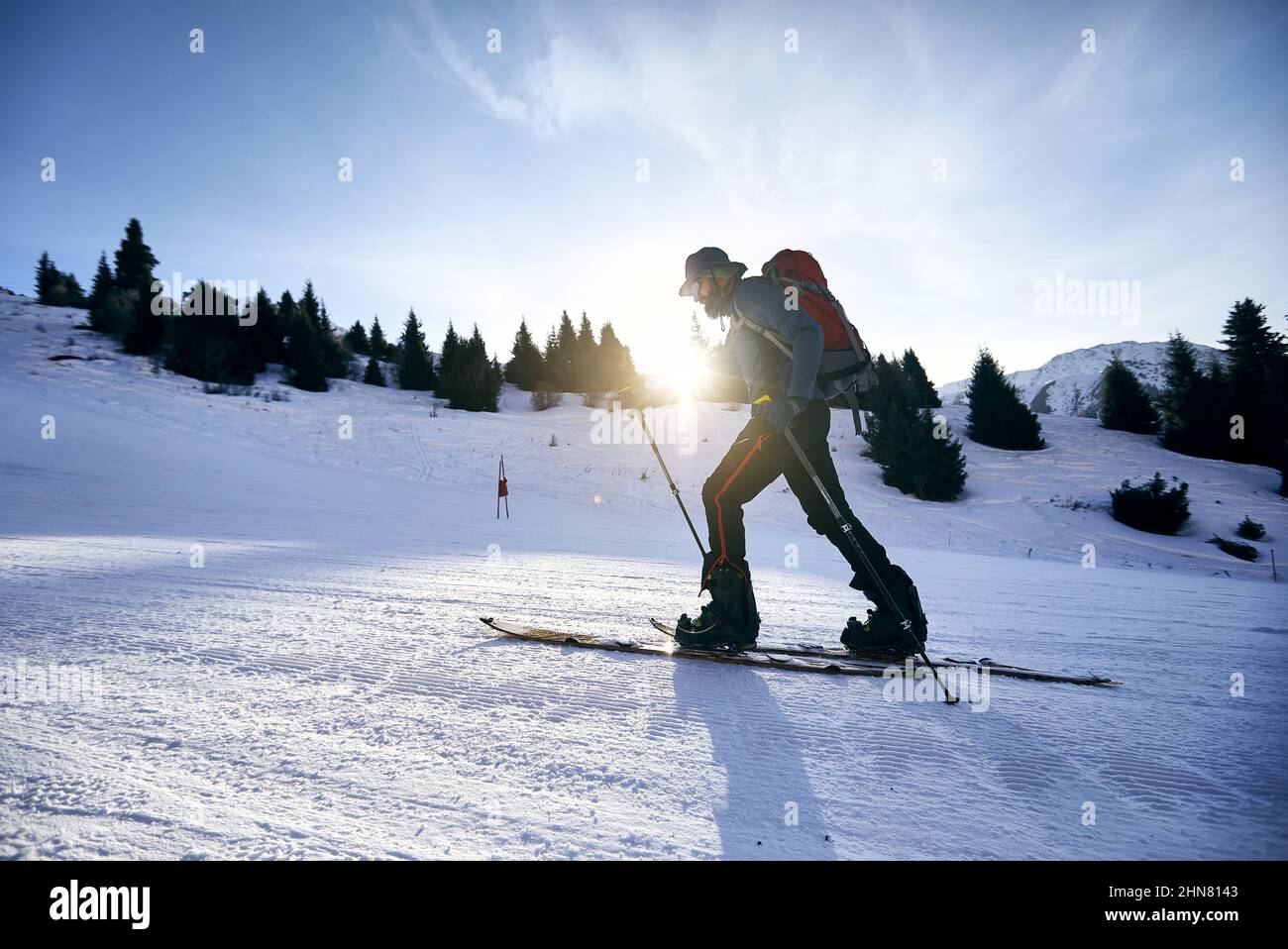 Skier man ski touring uphill with beard and backpack at high snowy mountain ski resort Shymbulak. Sport outdoor backcountry winter season. Stock Photo