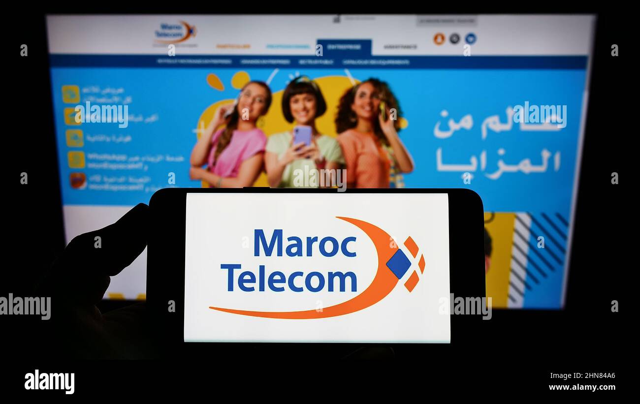 Person holding smartphone with logo of telecommunications company Maroc Telecom (IAM) on screen in front of website. Focus on phone display. Stock Photo