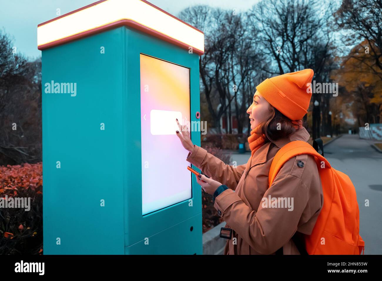 A woman uses a self-service kiosk to print photos from her smartphone on a city street Stock Photo