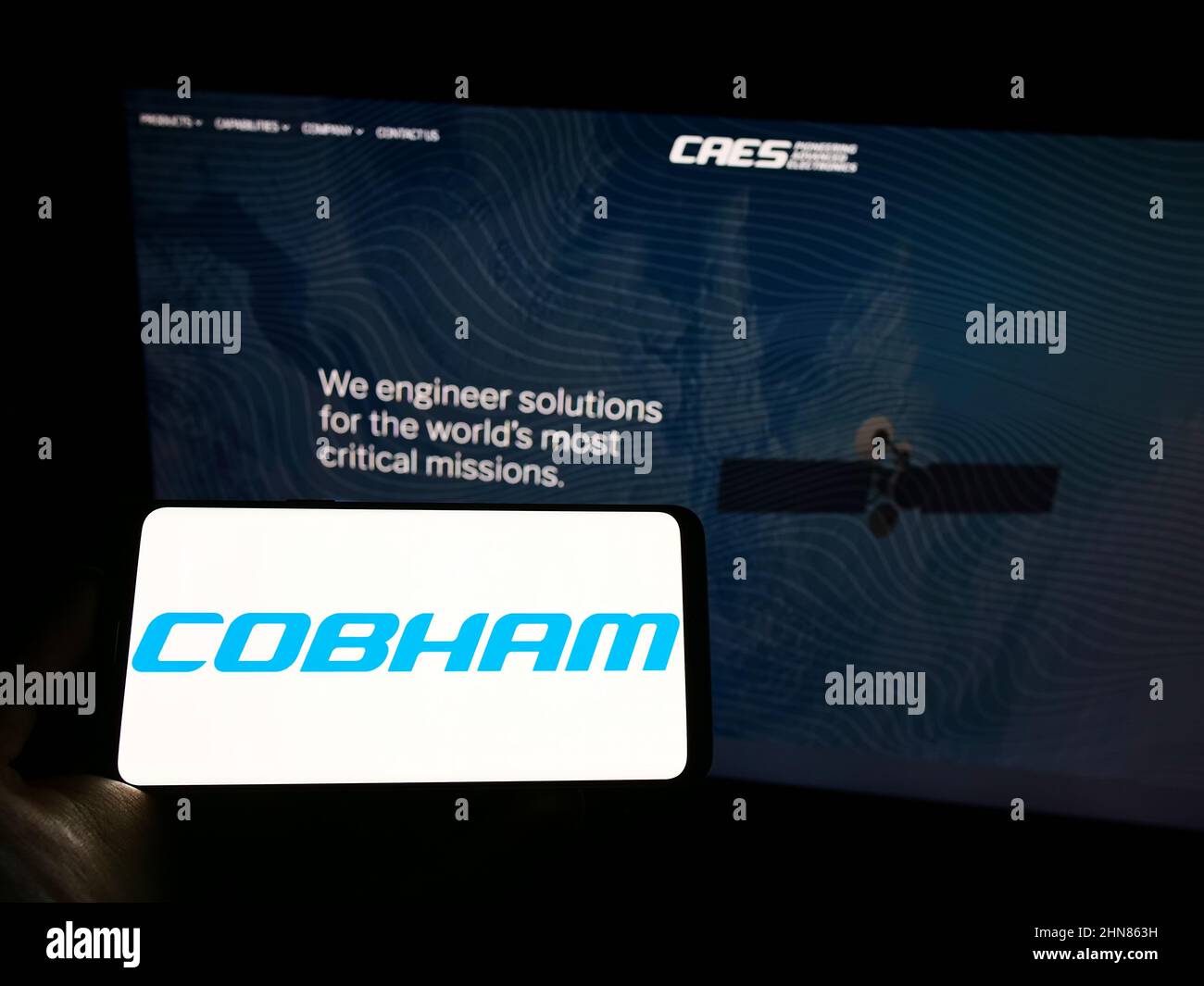 Person holding mobile phone with logo of British aerospace company Cobham Limited on screen in front of business webpage. Focus on phone display. Stock Photo