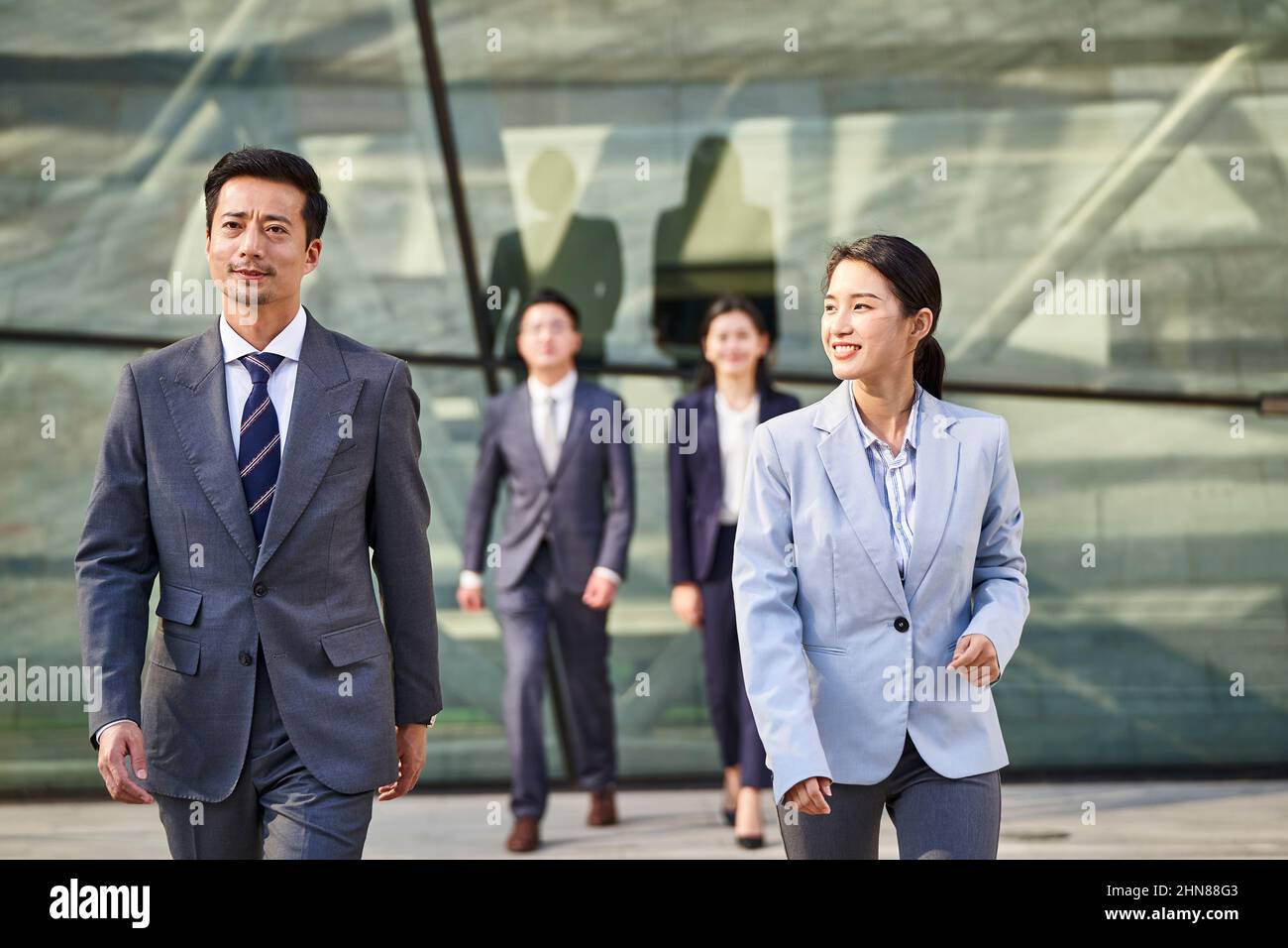 group of four young asian business people walking outdoors on street in modern city Stock Photo