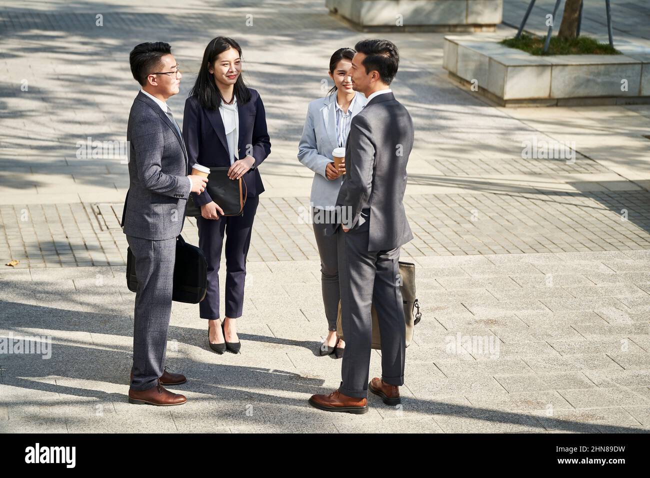 group of four young asian business people standing chatting outdoors on street Stock Photo