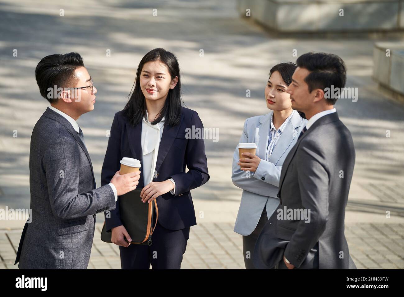 group of four young asian business people standing chatting outdoors on street Stock Photo