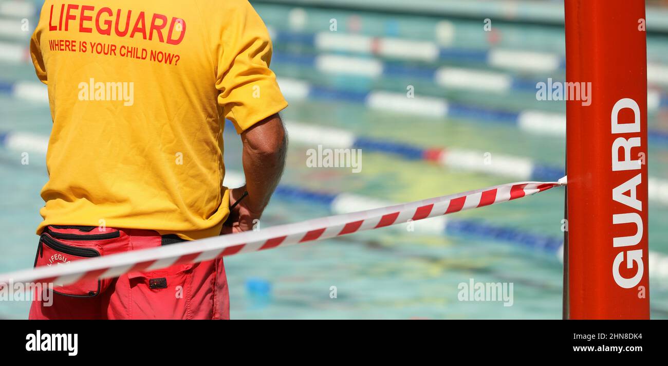 A public pool life guard or pool safety officer in uniform standing duty or guard supervising swimming and children preventing drowning accidents. Stock Photo