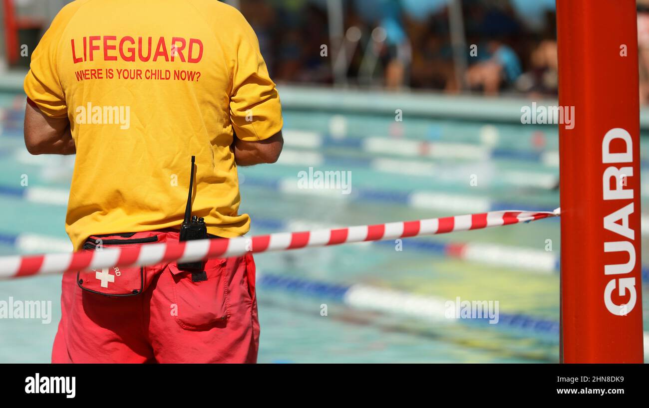 A public pool life guard or pool safety officer in uniform standing duty or guard supervising swimming and children preventing drowning accidents. Stock Photo