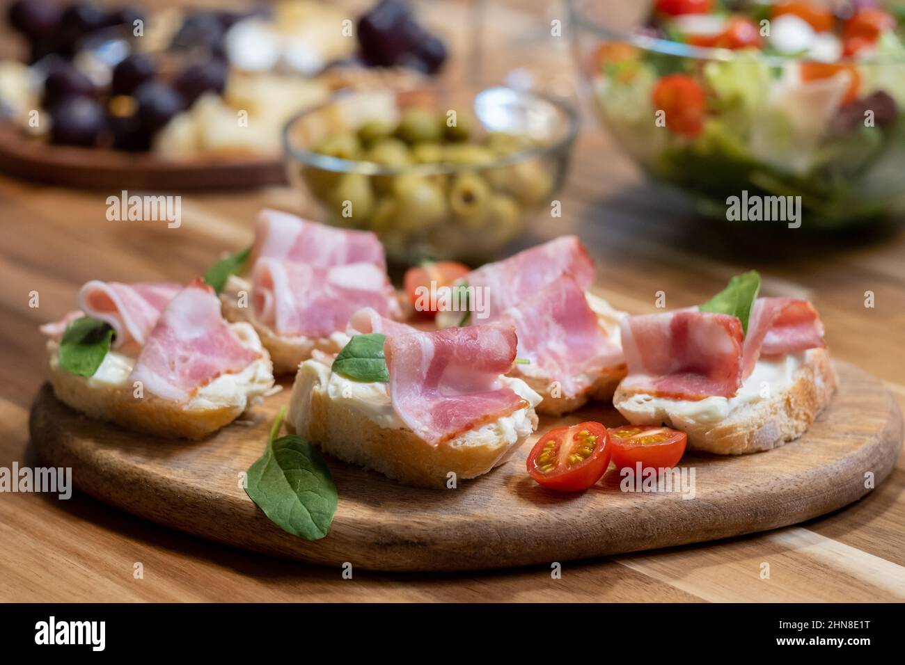 Close-up of sandwiches with bacon and tomatoes on wooden board on dining table Stock Photo