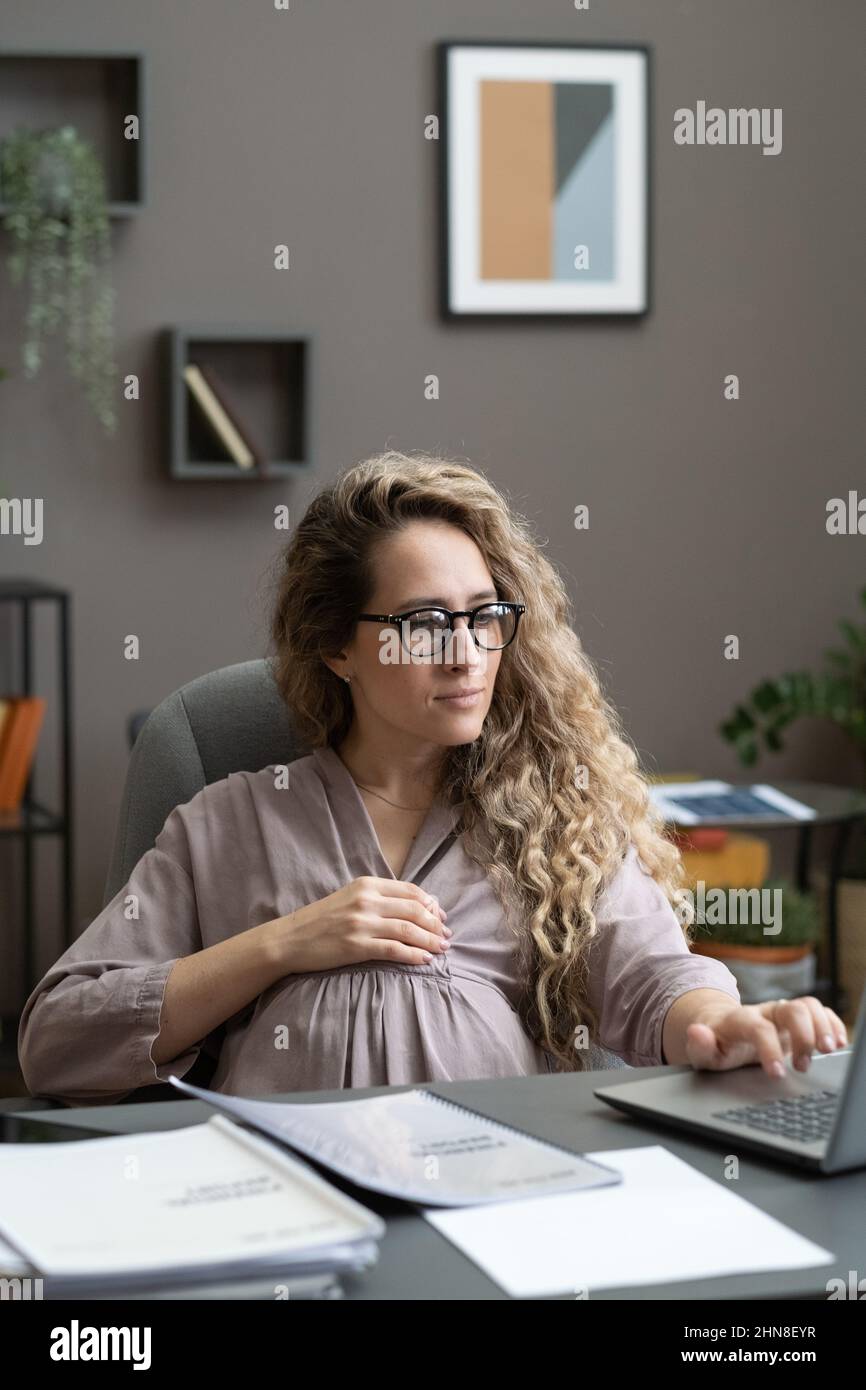 Young pregnant woman sitting at her workplace and typing on laptop