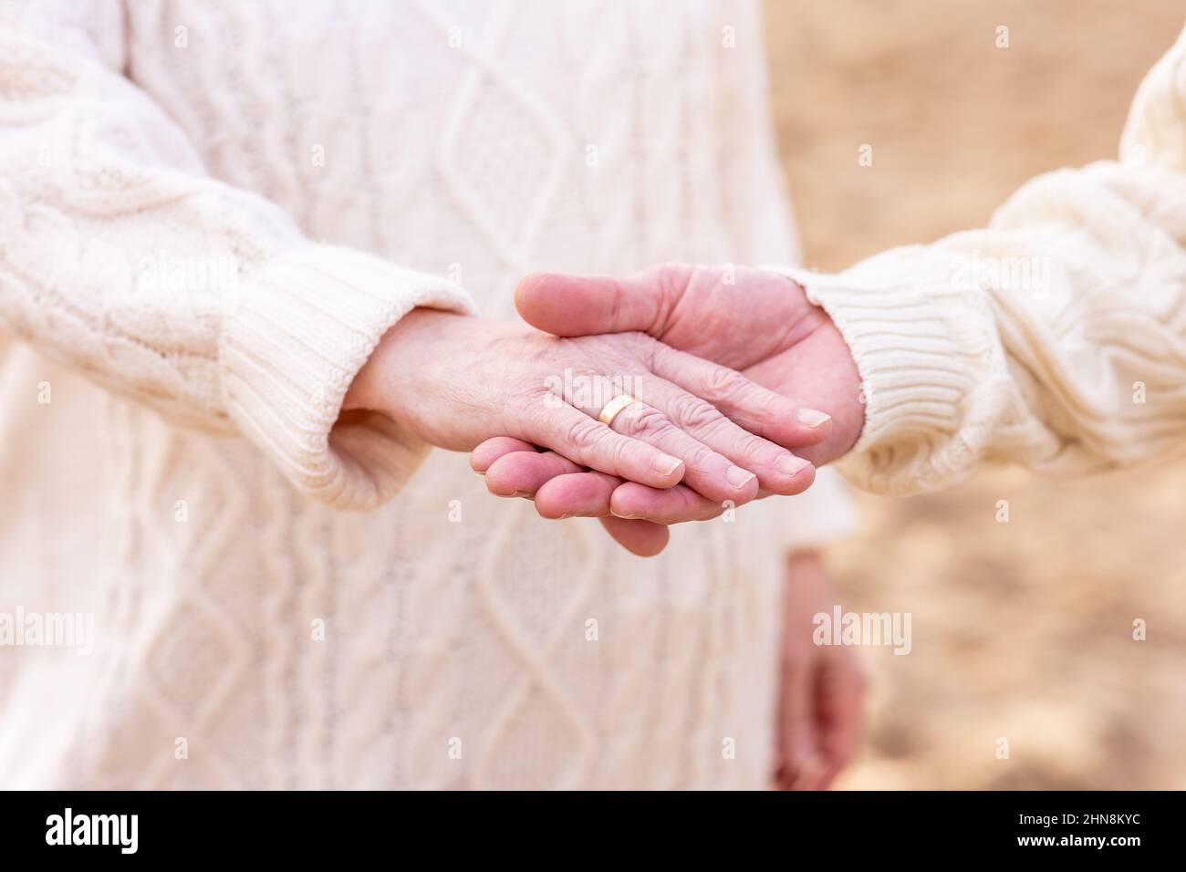 Closeup of the elderly couple. The man holding the woman's hand with a golden ring. Stock Photo