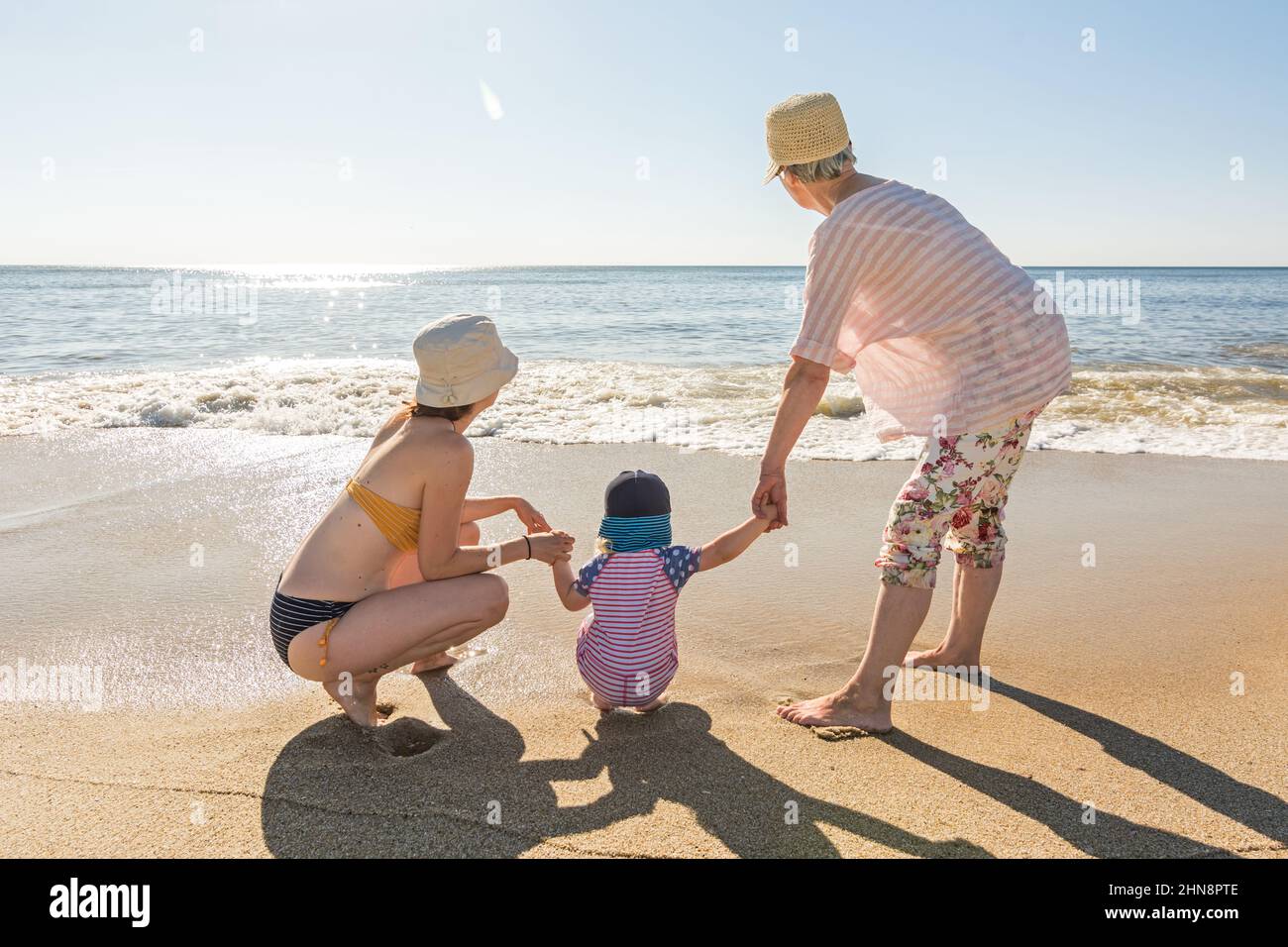 Family (grandmother, mother and daughter) holding hands at the beach in the evening sun Stock Photo