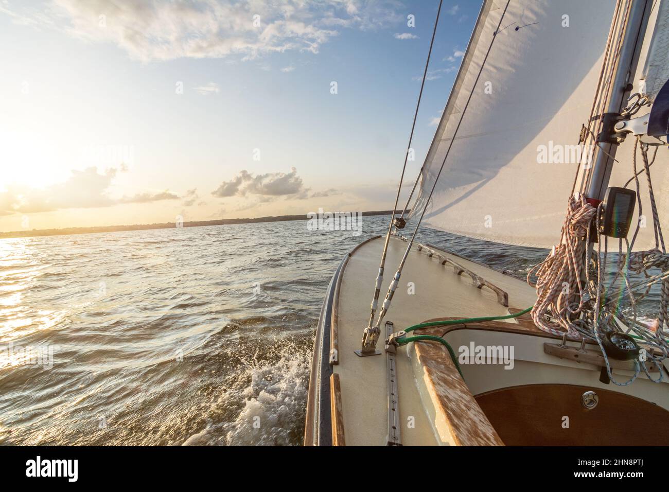 Sailing boat sailing fast into the sunset on choppy sea with slightly tilted horizon Stock Photo