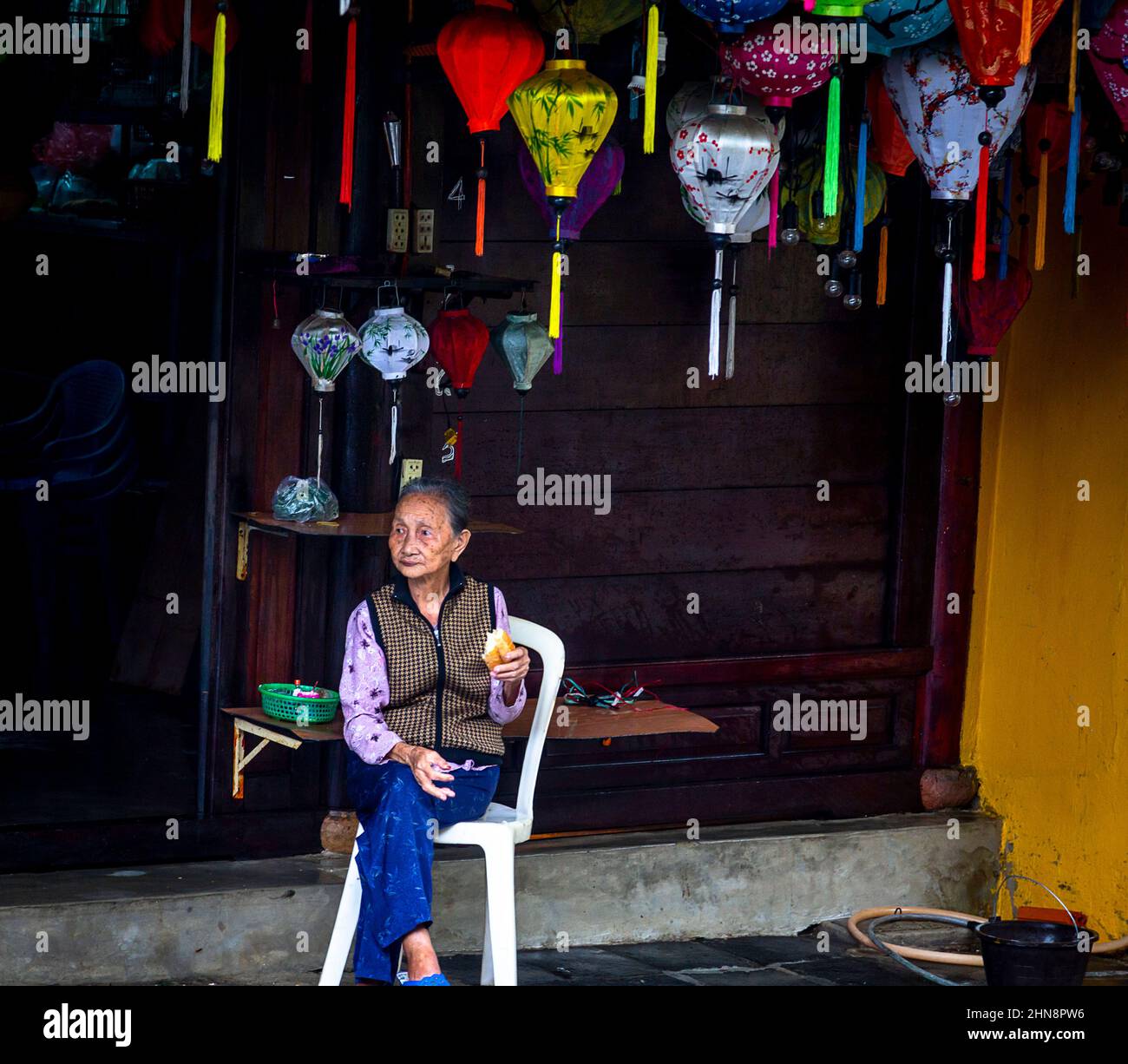 Under the lanterns is where this Vietnamese lady sits watching traffic go by in Old Town, Hoi An. Stock Photo
