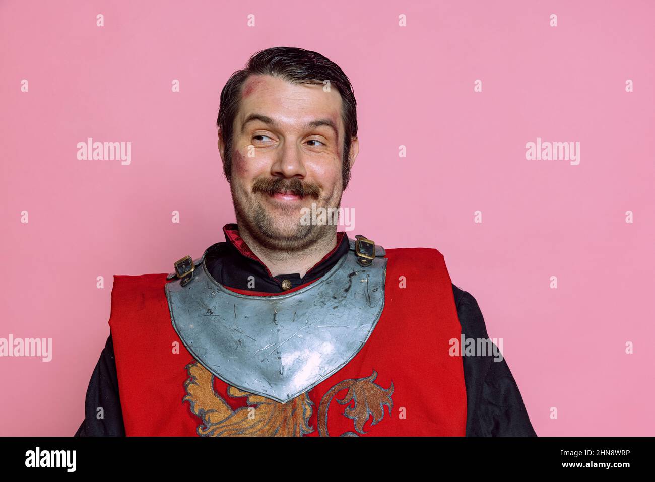 One young man, medieval warrior or knight wearing wearing armor clothing posing isolated over pink background. Comparison of eras, history, emotions Stock Photo