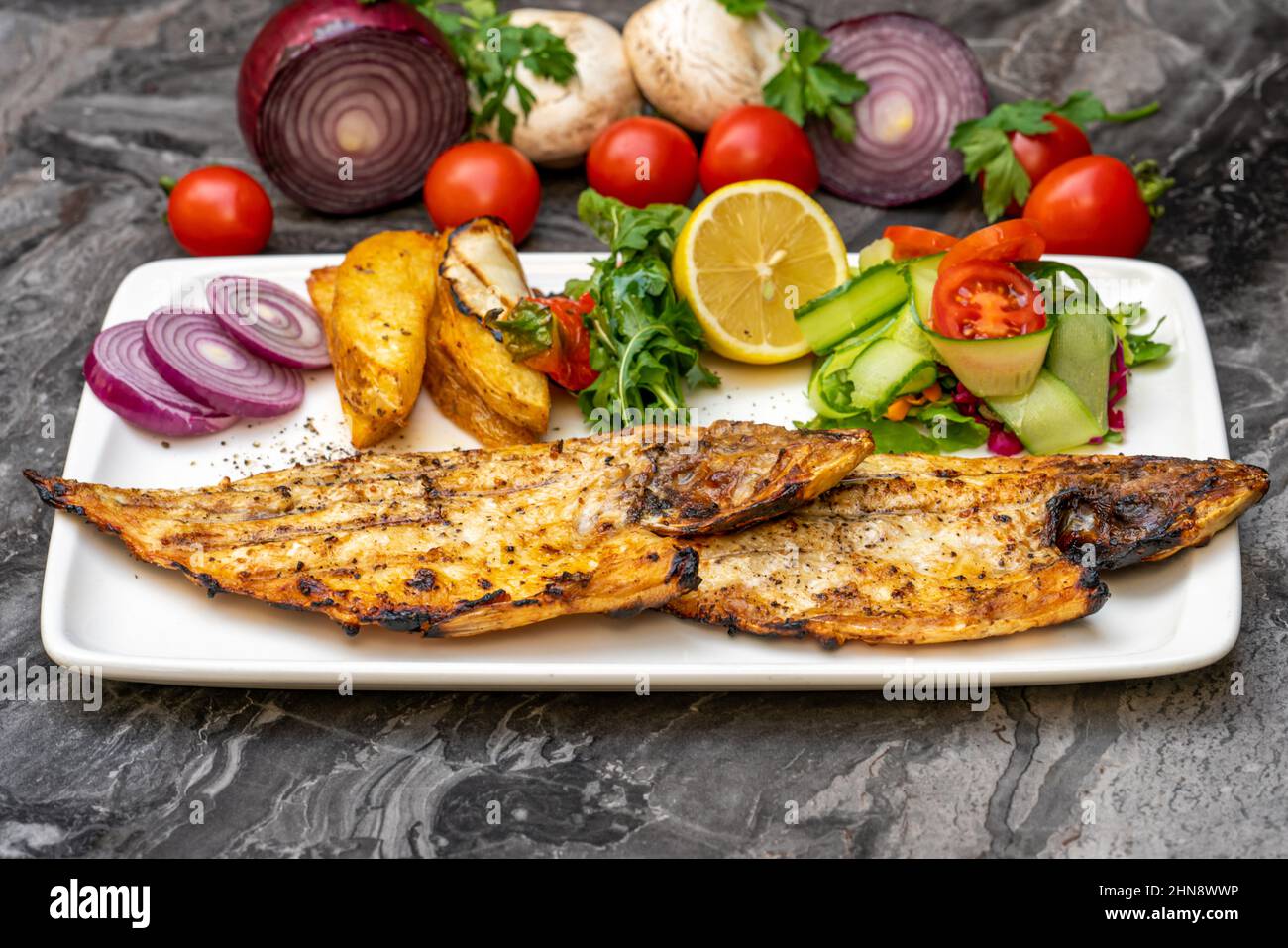 Grilled sea bream with salad and french fries on the dark table Stock Photo