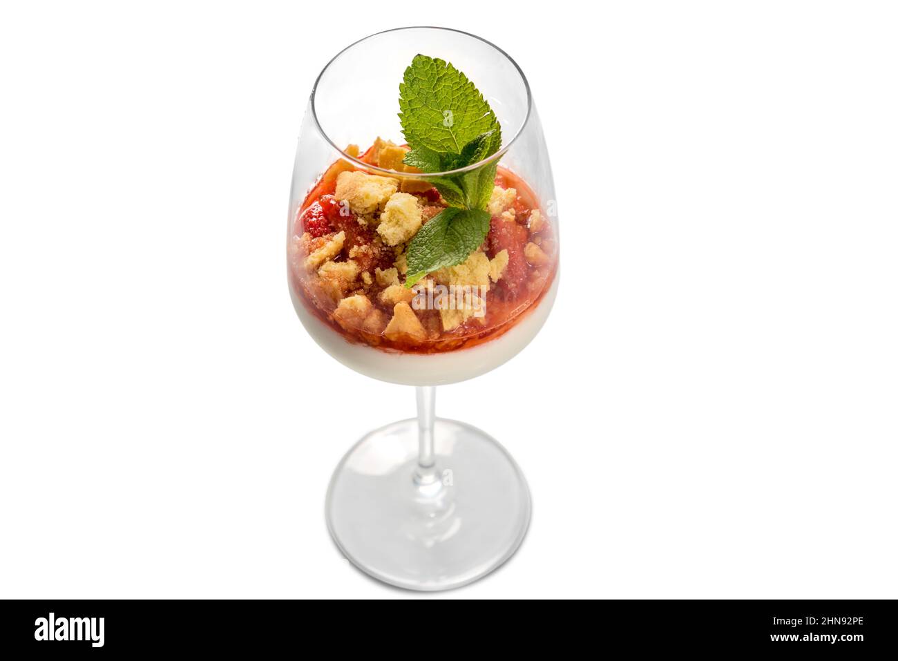 Panna cotta italian dessert with strawberry syrup and crumbled cake with mint leaves in glass goblet glass, top view, isolated on white Stock Photo