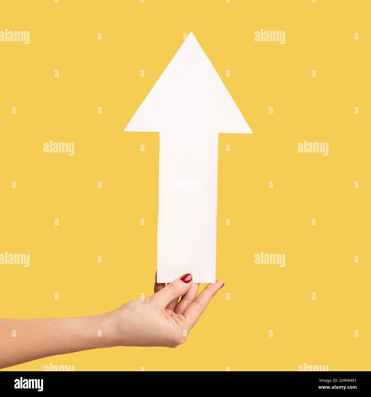 Closeup profile side view of woman hand holding arrow pointing up, growth and increase concept. Indoor studio shot isolated on yellow background. Stock Photo