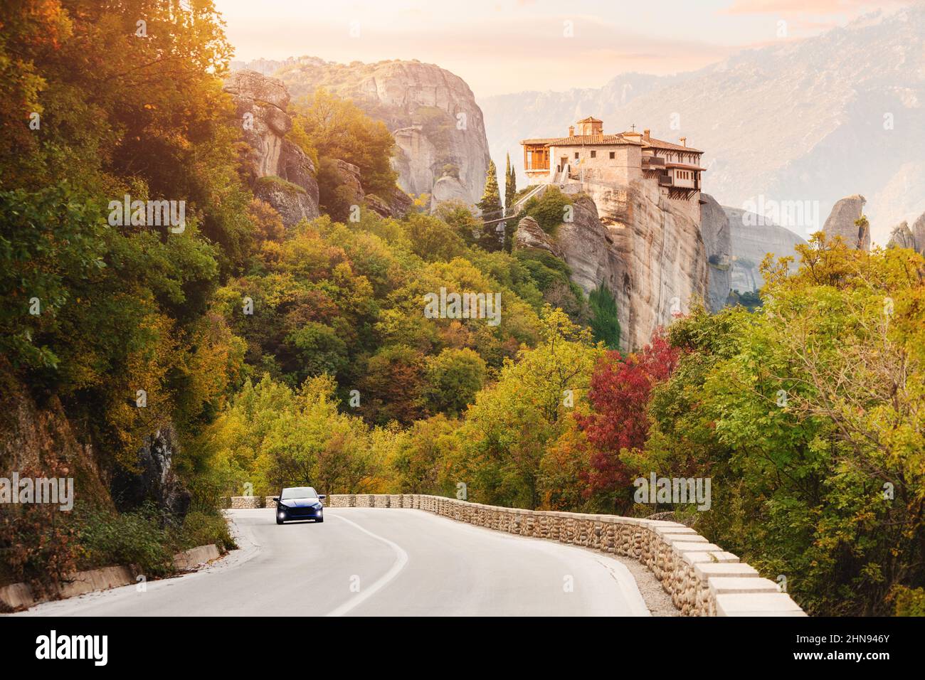 Inspirational view of iconic and majestic Saint Barbara Meteora monastery and car driving on a winding road in Greece. Discover new tourist experience Stock Photo