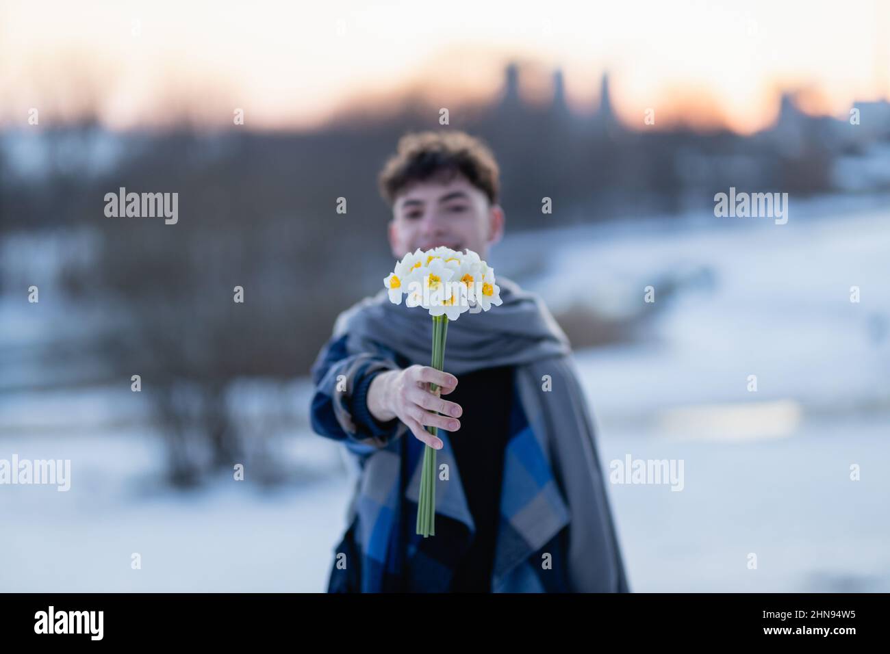 Portrait of a young man  against the backdrop of an industrial landscape in winter. Man holding a bouquet of daffodils. Selective focuse on flowers. Stock Photo