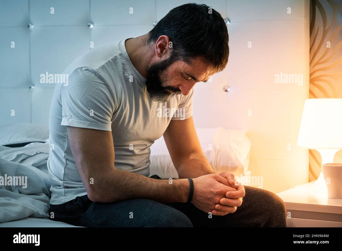 Person with some kind of problem sitting on the bed and with his head bowed. Stock Photo