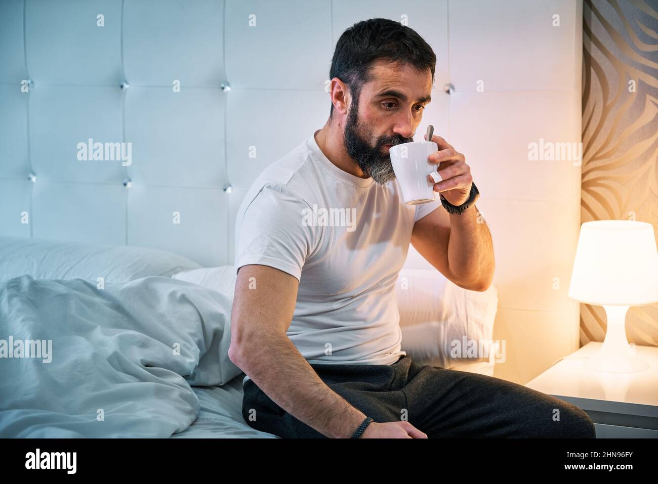 person with some kind of problem sitting on the bed and drinking from a cup Stock Photo