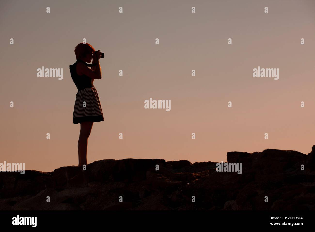 silhouette of young woman photographer, taking pictures of landscape at sunset Stock Photo