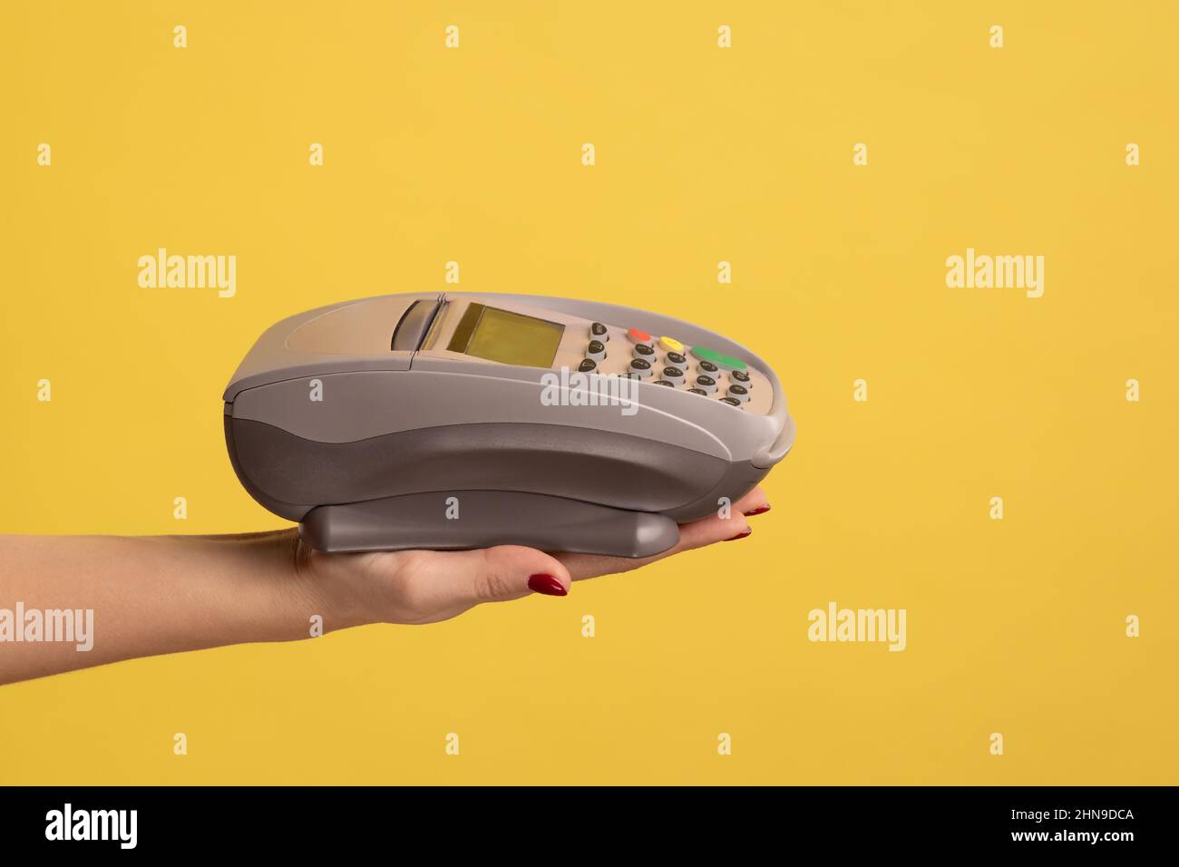Profile side view closeup of woman hand holding POS or terminal payment or pay pass device. Indoor studio shot isolated on yellow background. Stock Photo