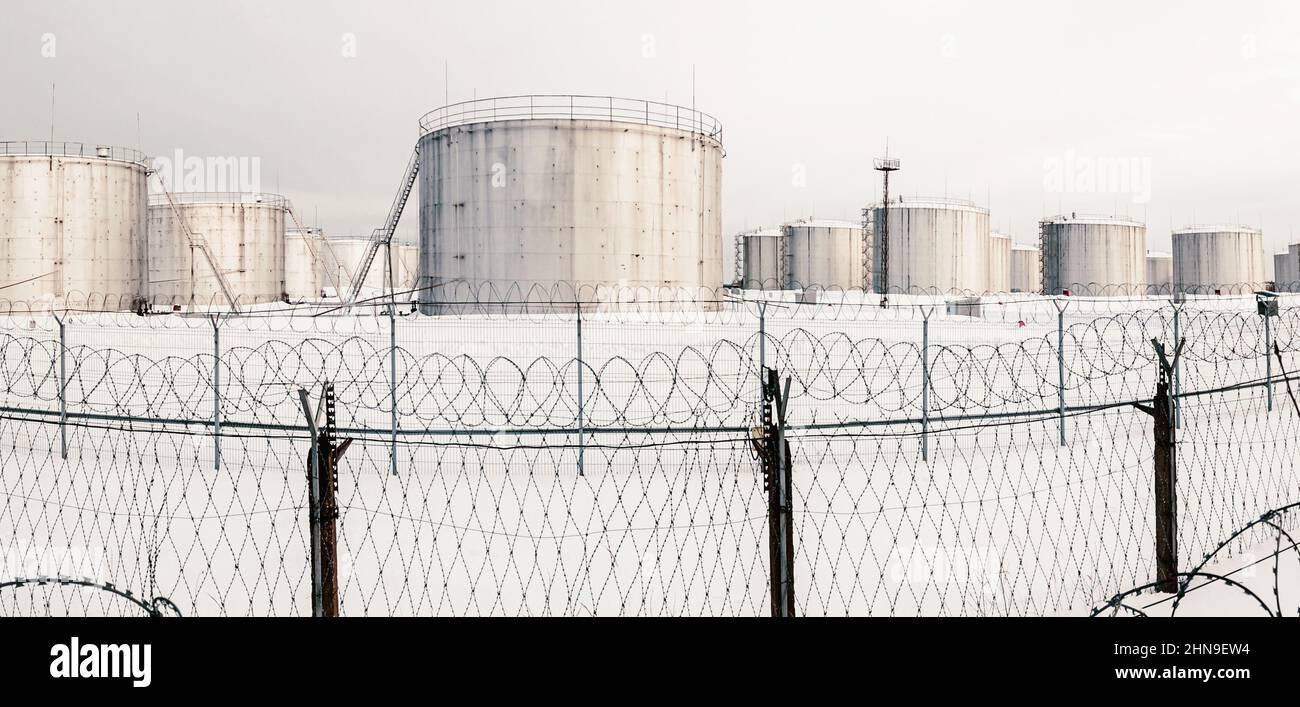Gas storage tanks in winter, tank farm behind a fence topped with barbed wire Stock Photo