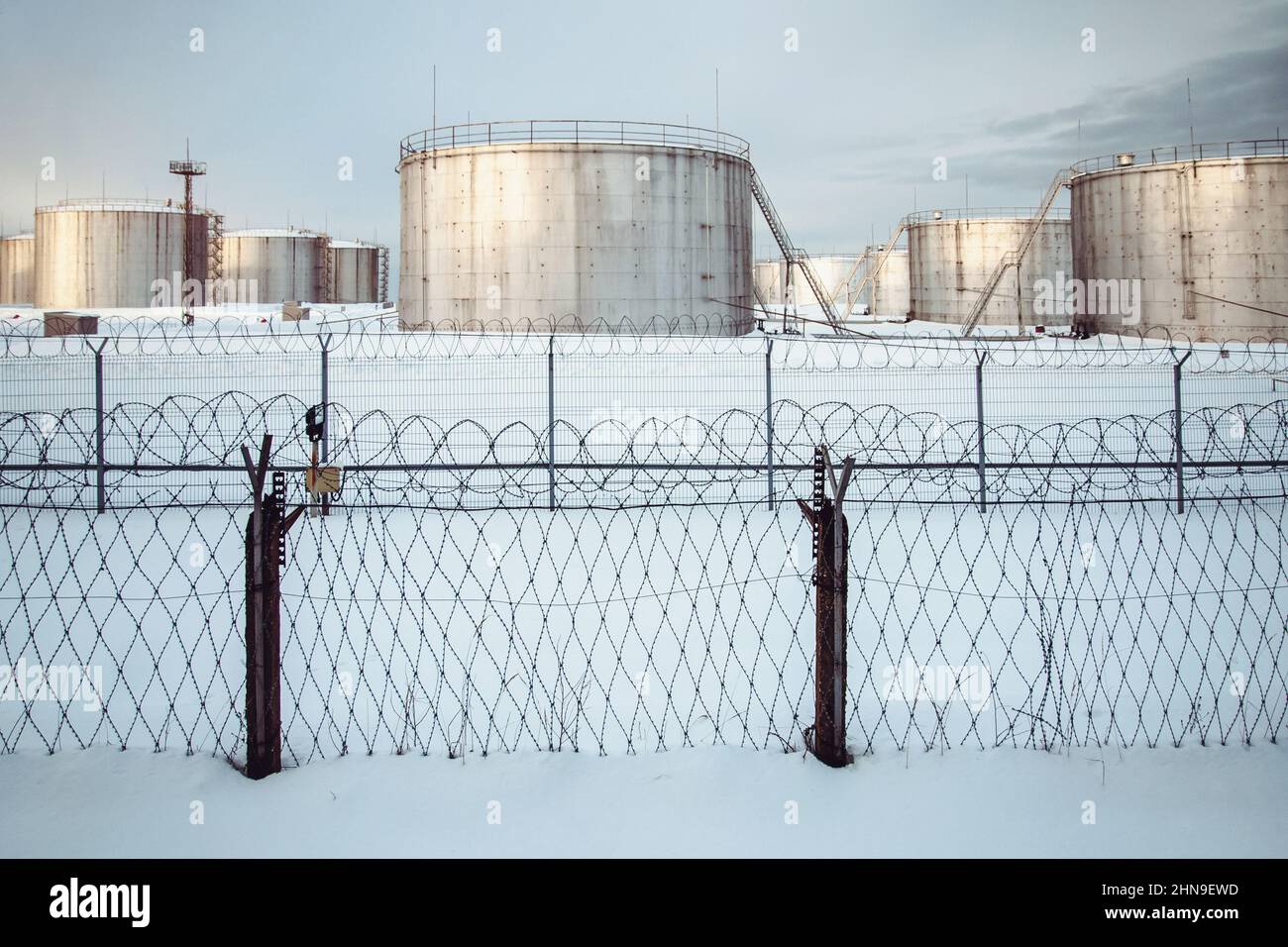 Tank farm of oil storage terminal secured with fence, winter view, snow Stock Photo