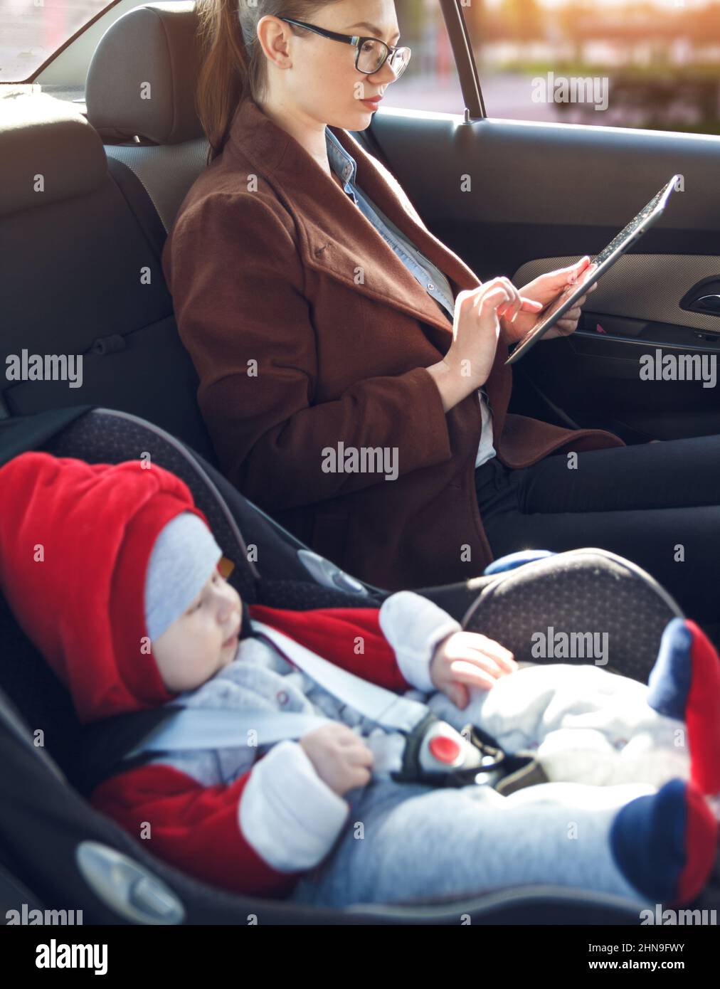 Mother with her small child in a baby car seat ride in the back seat of a taxi Stock Photo