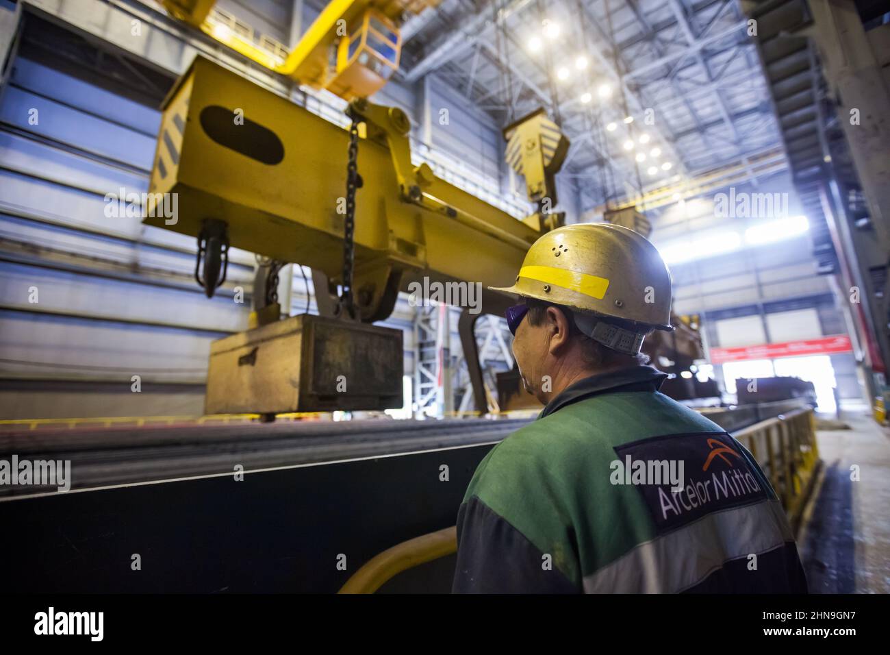 Temirtau, Kazakhstan - June 08, 2012: Arcelor Mittal metallurgy plant. Worker  with conveyor belt and crane. Lifting magnet WOKO for square bar metal. Stock Photo