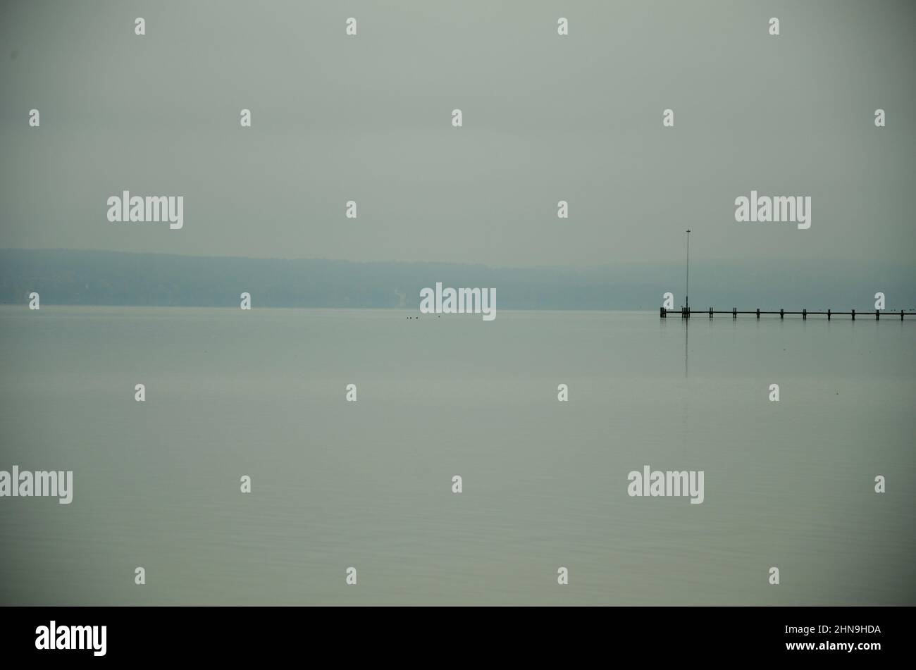 A long lonely footbridge reaches into the foggy Ammersee in Bavaria. Mountain ranges on the horizon Stock Photo
