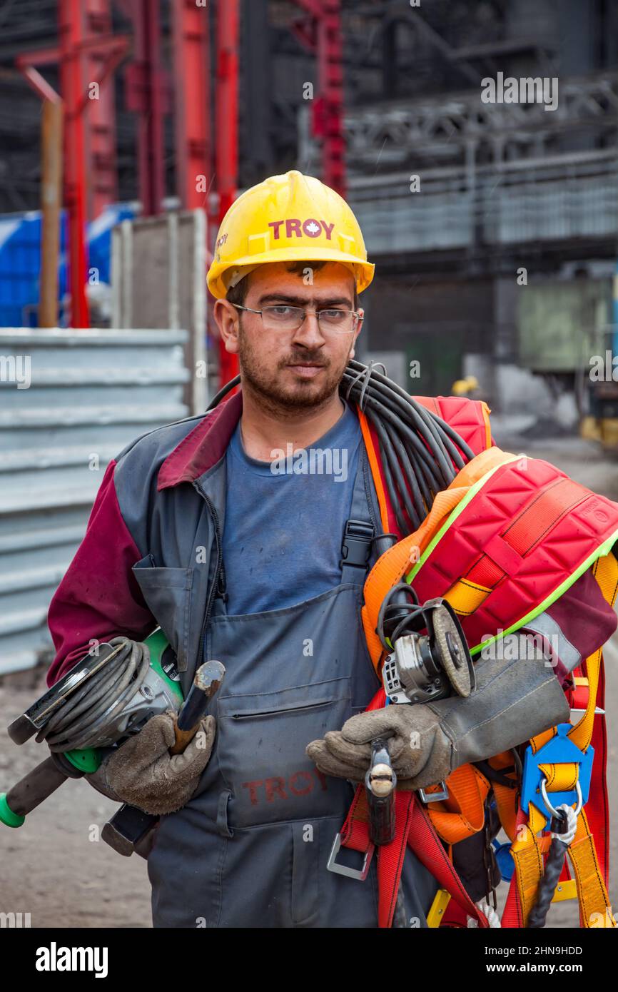 Temirtau, Kazakhstan - June 08, 2012: Arcelor Mittal metallurgy plant. Industrial climber in yellow hardhat with safety belts and angle grinder tool. Stock Photo