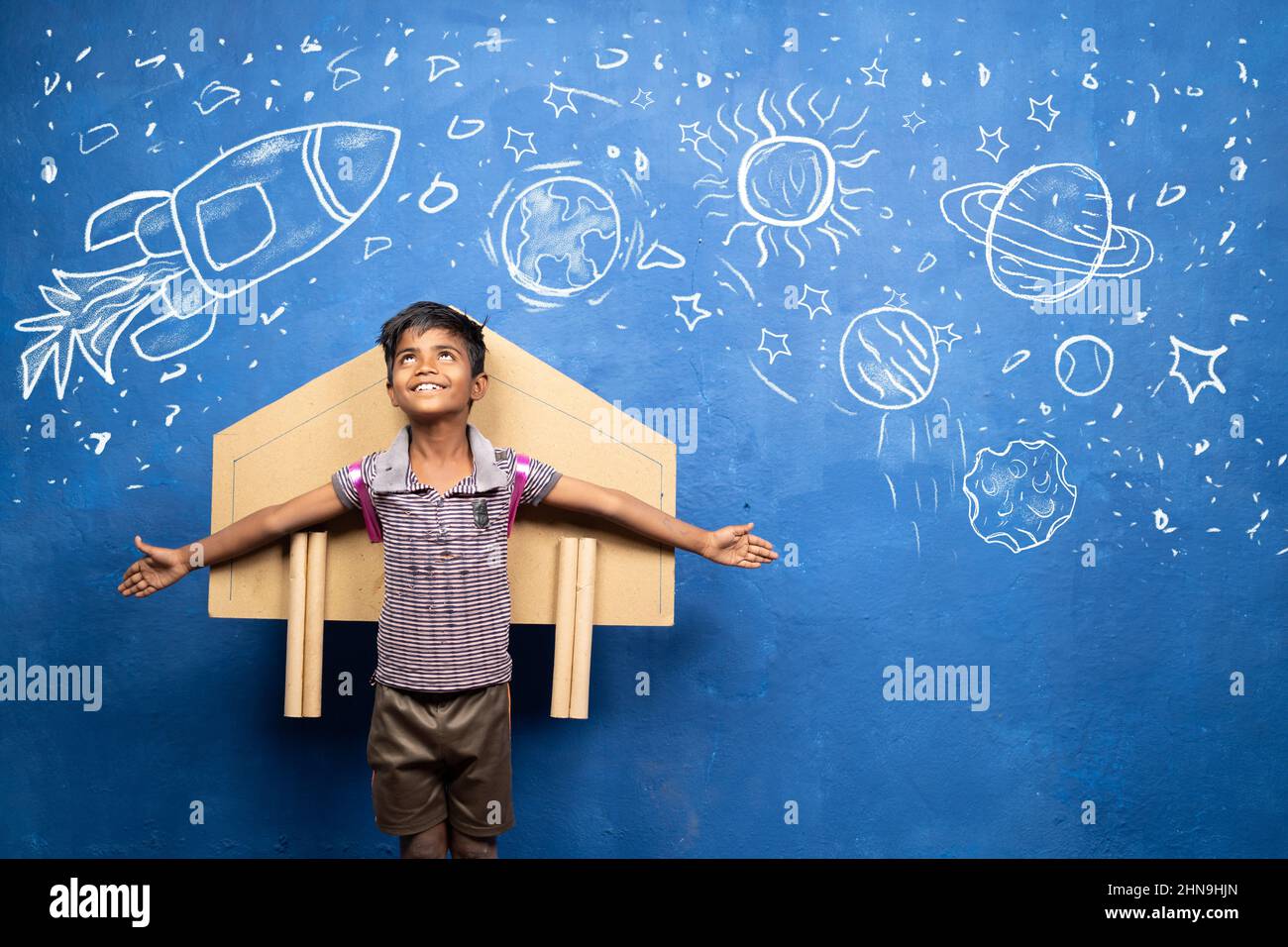 happy kid with cardboard rocket on back with space, universe and planets doodle drawing on wall - concept showing of childhood dream about astronaut Stock Photo