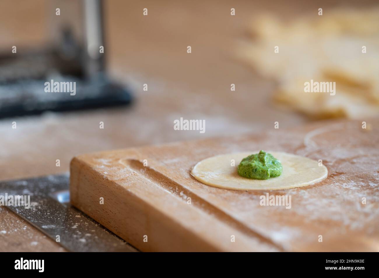 round baking dish with portion of spinach mass for original tyrolean dumplings schlutzkrapfen in kitchen with wooden board full of flour Stock Photo