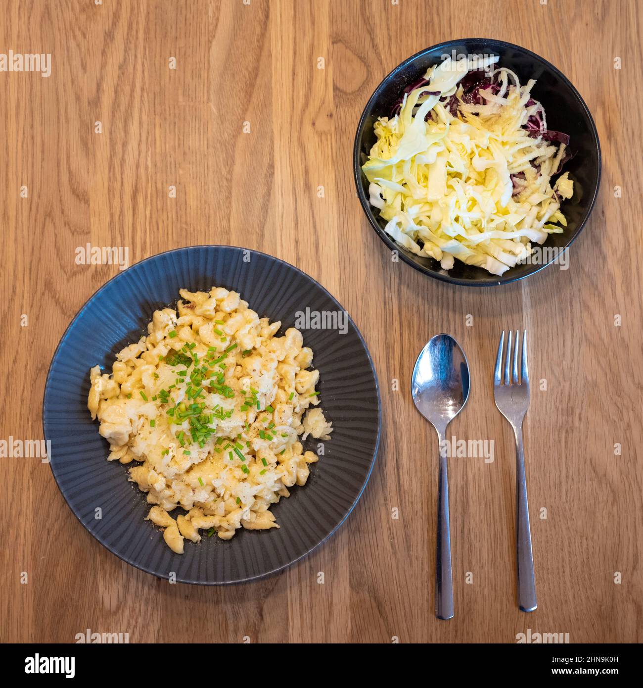 Cheese spaetzle with onion and chives served with coleslaw bowl on wood table Stock Photo