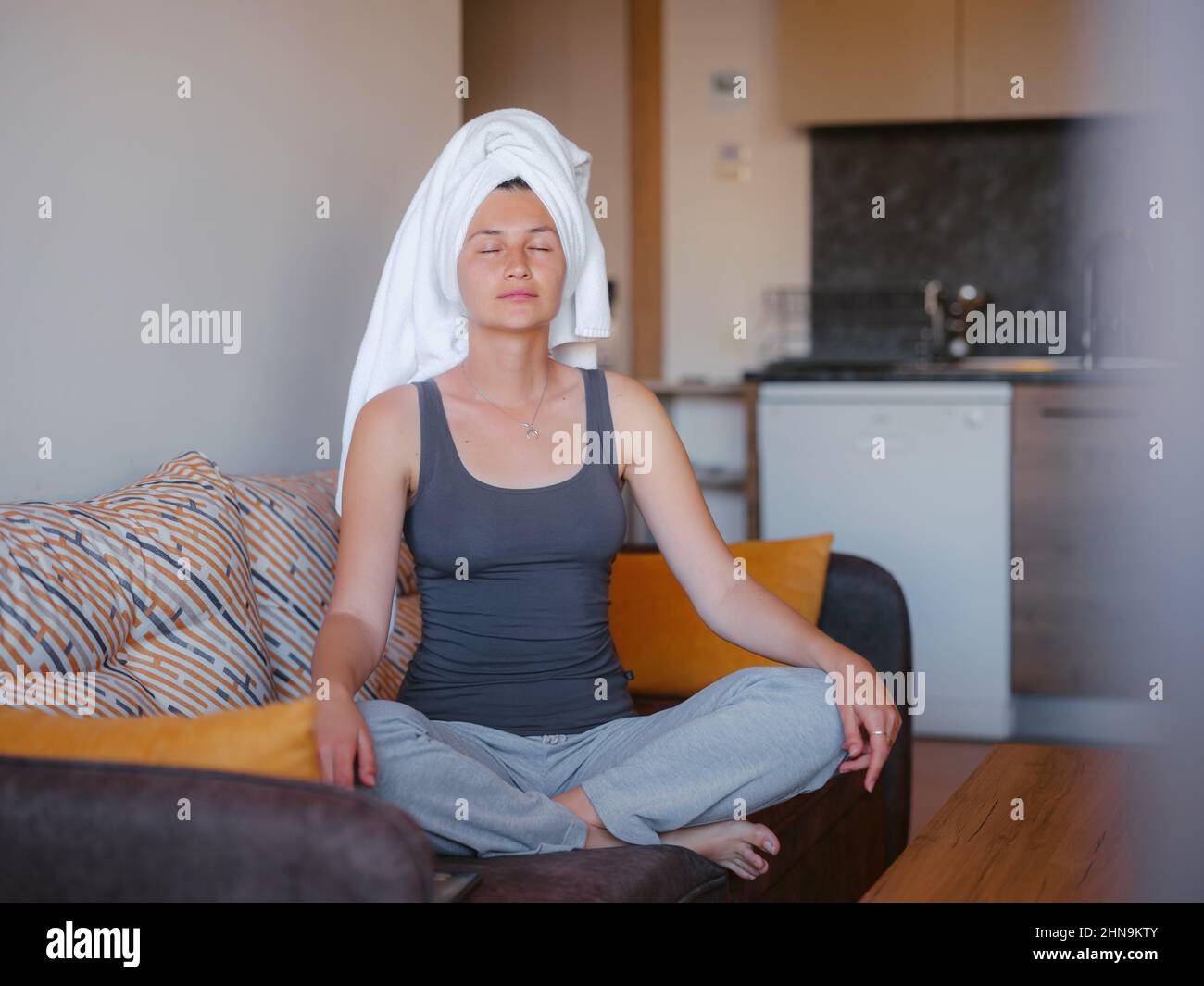 woman sitting on sofa, lotus position puts hands on knees, closed eyes, enjoy meditation, do yoga. No stress, healthy habits, conscious lifestyle, anxiety relief concept Stock Photo