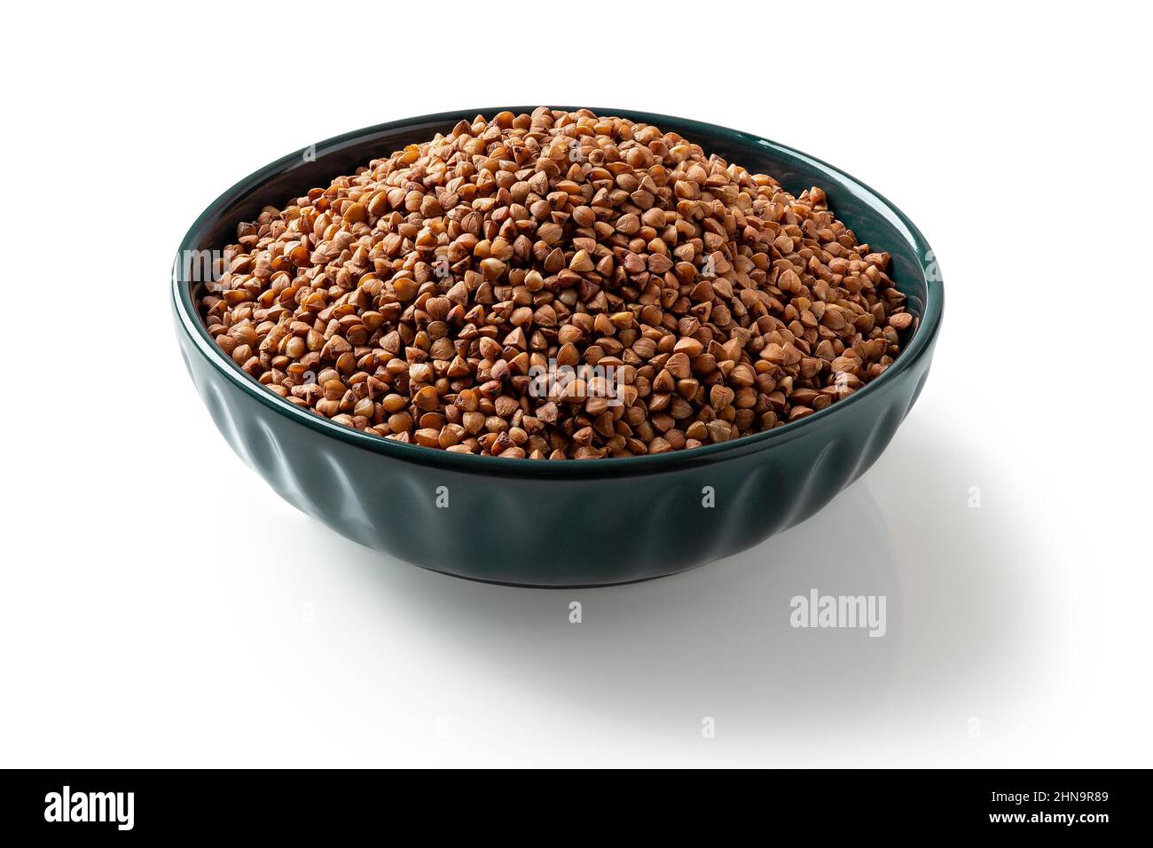 Raw wholegrain buckwheat groats in a blue bowl isolated on a white background. Roasted organic buckwheat grains for gluten free diet. Vegetarian food. Stock Photo
