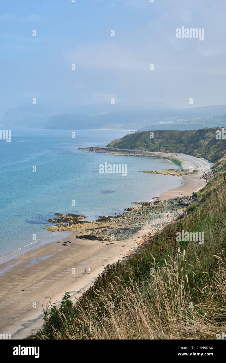 Two distant people walk along the otherwise deserted Eastern end of Porth Dinllaen Beach, Wales on a bright but hazy day. Stock Photo