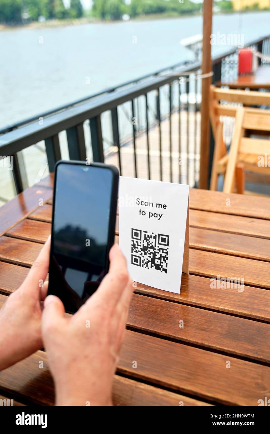 Hands of an unrecognizable client scanning a QR code with a smartphone to pay the restaurant bill using contactless, cashless digital technology. Stock Photo