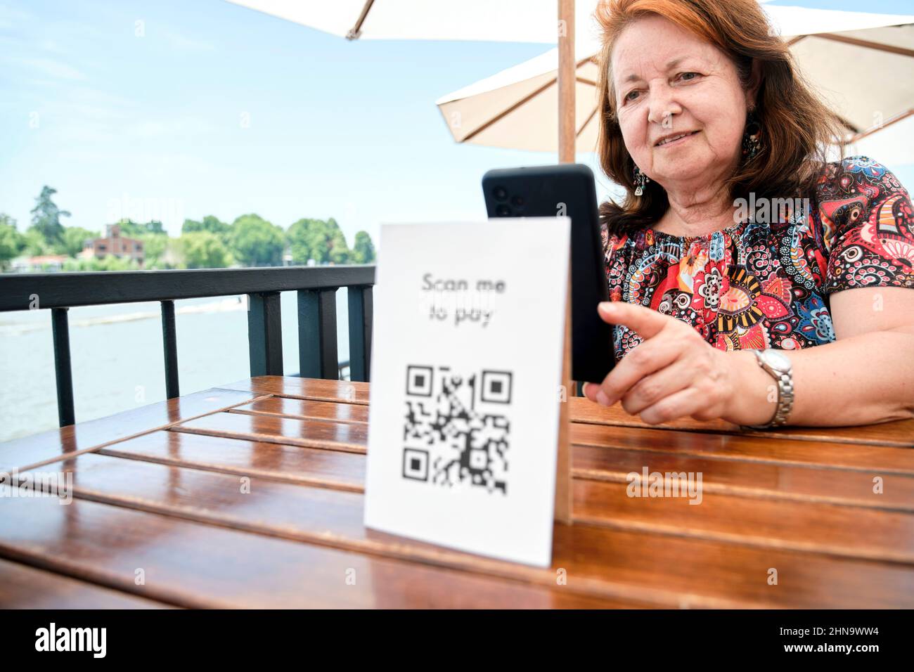 Mature hispanic woman scanning a QR code with her smartphone to pay her restaurant bill using contactless, cashless technology. Focus on the female cl Stock Photo