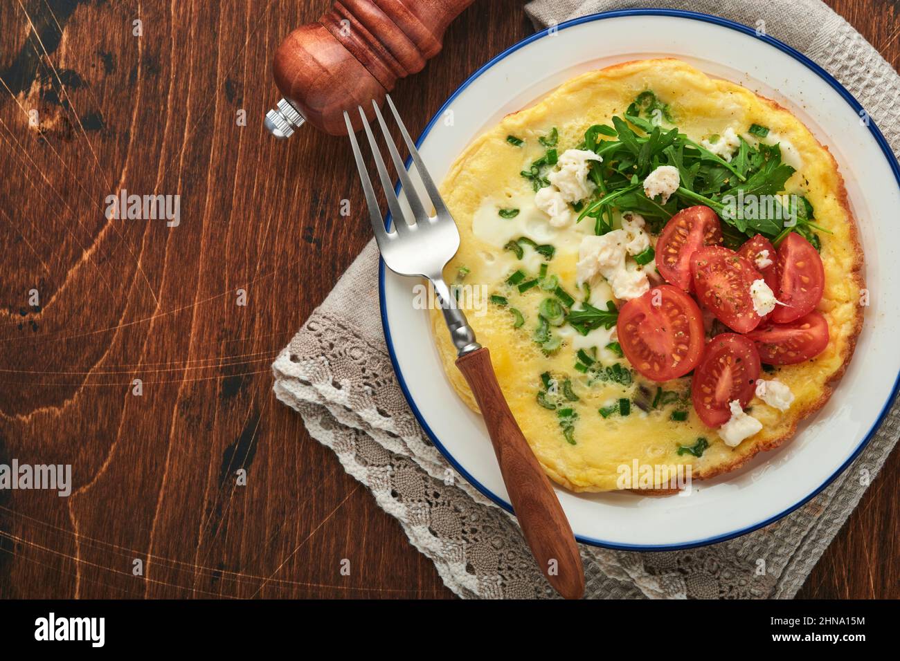 Rustic omelette or frittatas with green onions, cheese mozzarella, green arugula and tomatoes on old wooden dark background. Healthy food concept. Bre Stock Photo