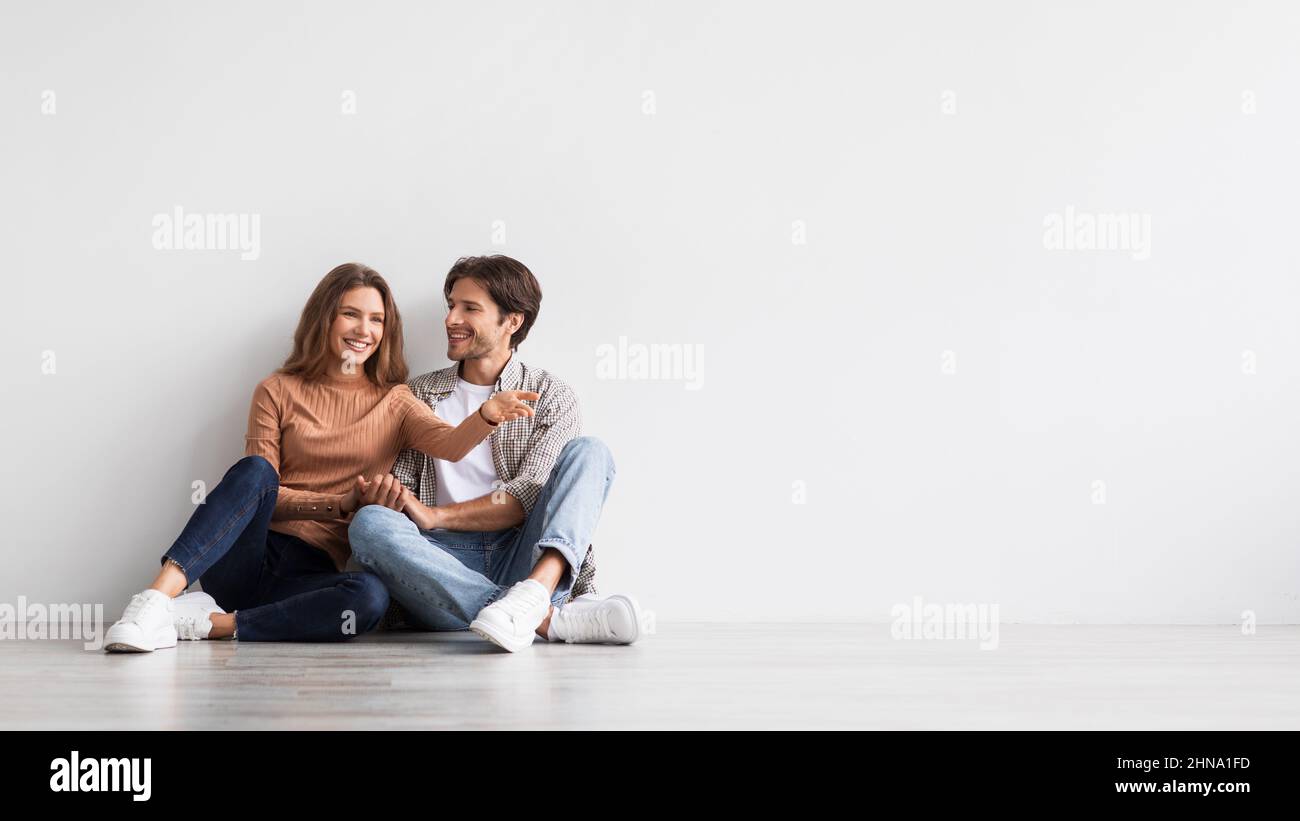 Glad young european man and lady planning future interior in first home, dream, sit on floor on white wall background Stock Photo