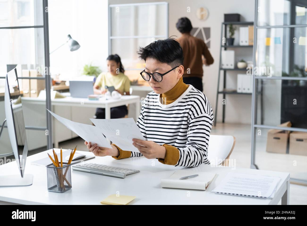Asian young businesswoman in eyeglasses sitting at her workplace at office and examining the documents, she reading a contract Stock Photo