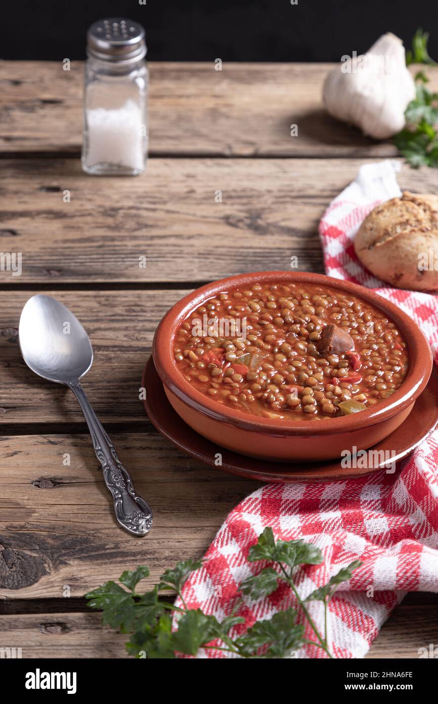 Homemade lentil soup with ingredients on a wooden background. Vertical format. Traditional Spanish dish concept. Stock Photo