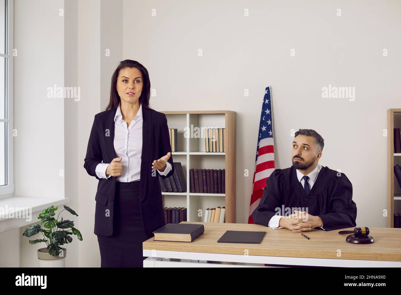 Female lawyer or defense attorney speaking to judge and audience during court trial Stock Photo