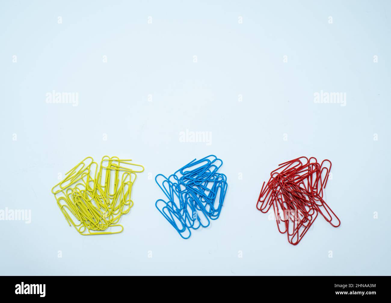 Multi coloured, blue, red and yellow paper clips in piles on a plain white background. Stock Photo