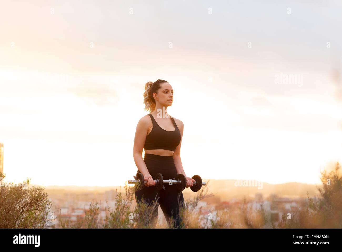 Young fitness woman lifts weights outdoors at sunset Stock Photo Alamy