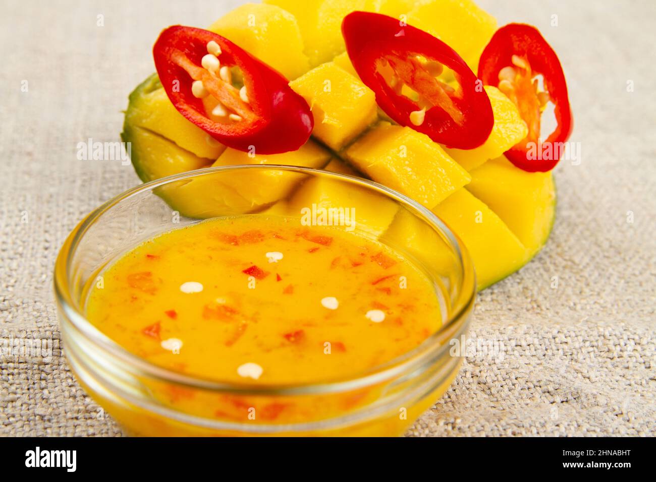 Close-up of diced half of mango, sliced red hot pepper and mango chili sauce on burlap. Rustic style. Soft focus Stock Photo
