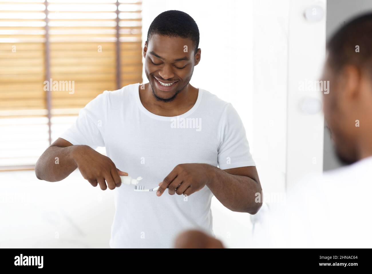 Handsome Black Man Applying Toothpaste On Toothbrush Near Mirror In ...